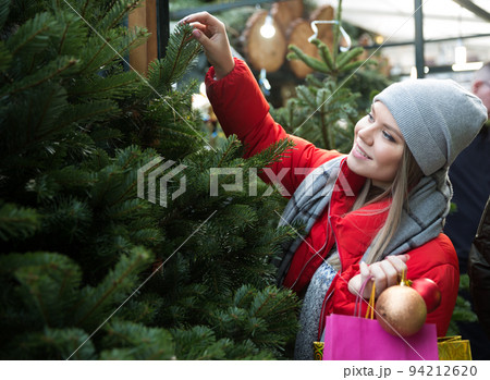Happy young woman chooses a Christmas tree on the street market 94212620