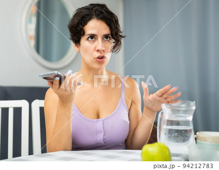 Upset woman sitting at table and having telephone conversation 94212783