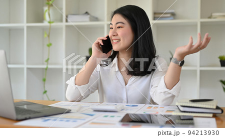 Successful Asian businesswoman at her office desk talking on the phone with her partner. Successful Asian businesswoman at her office desk talking on the phone with her partner. 94213930