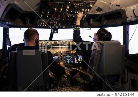 Aircrew members flying airplane with dashboard command, using control panel and navigation windscreen. Piloting aircraft with power lever switch and handle in aviation cockpit cabin. Aircrew members flying airplane with dashboard command, using control panel and navigation windscreen. Piloting aircraft with power lever switch and handle in aviation cockpit cabin. 94215144
