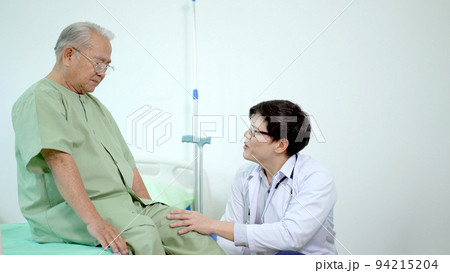 Elder Asian man sitting on the bed and talking to doctor about his physical injuries at his knees, elderly Asian man having a consulting with professional physical therapist or orthopedic doctor. Elder Asian man sitting on the bed and talking to doctor about his physical injuries at his knees, elderly Asian man having a consulting with professional physical therapist or orthopedic doctor. 94215204