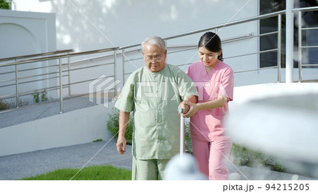Senior elder Asian man having a physical therapy by walking with cane staff support. Professional caregiver taking an elder Asian old man walking at the park. Senior elder Asian man having a physical therapy by walking with cane staff support. Professional caregiver taking an elder Asian old man walking at the park. 94215205