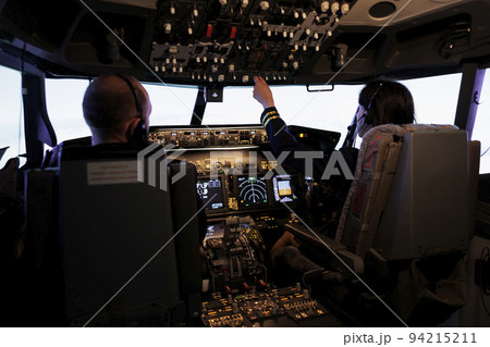 Woman copilot assisting captain to takeoff and fly airplane, using buttons on dashboard command in pilot cockpit. Airliners flying plane jet with navigation windscreen and control panel. Woman copilot assisting captain to takeoff and fly airplane, using buttons on dashboard command in pilot cockpit. Airliners flying plane jet with navigation windscreen and control panel. 94215211