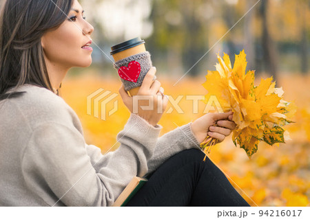 Young mixed race woman drinking coffee in autumn park Young mixed race woman drinking coffee in autumn park 94216017