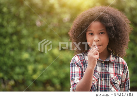 Happy African-American kid girl with a lollipop in her hands in the garden or outdoors. 94217383