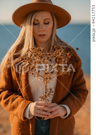 A woman walking along the coast near the sea. An elegant lady in a brown coat and a hat with fashionable makeup walks on the seashore A woman walking along the coast near the sea. An elegant lady in a brown coat and a hat with fashionable makeup walks on the seashore 94217755