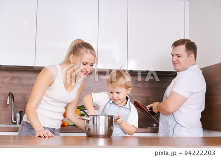 Family mom son, dad are preparing delicious food in kitchen. Mom teaches Family mom son, dad are preparing delicious food in kitchen. Mom teaches 94222203