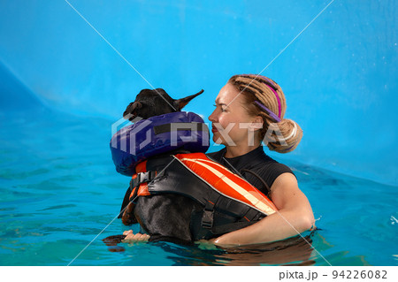 Dog in life jacket swim in the swimming pool with coach. Pet rehabilitation. Recovery training prevention for hydrotherapy. Pet health care 94226082