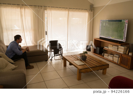 Man with a disability watching football match and sitting on the couch Man with a disability watching football match and sitting on the couch 94226166