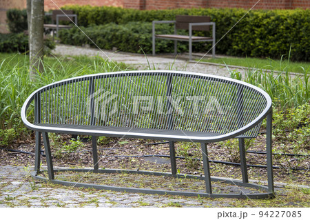 Modern metal bench in public city park at summer. Green park with benches for rest, empty bench. Modern metal bench in public city park at summer. Green park with benches for rest, empty bench. 94227085