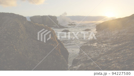 Image of red, white and blue squares and crossed american flags over rocks and ocean at sundown Image of red, white and blue squares and crossed american flags over rocks and ocean at sundown 94227580