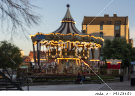 Abstract blurred background of vintage carousel. Unfocused lights of a Merry-go-round or carousel with orange illumination, blurred lights. Gdansk, Poland. 94228339