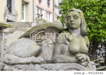 Sphinx sculpture, a fusion of a lion and a woman made from stone on the street of Old Town in Gdansk, Poland. Mysterious woman sphinx statue lies near old building in the park 94228383