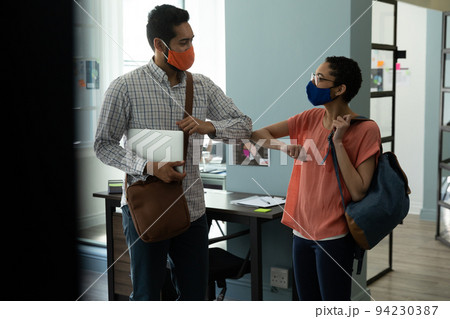 Mixed race man and woman wearing masks bumping elbows in greeting Mixed race man and woman wearing masks bumping elbows in greeting 94230387