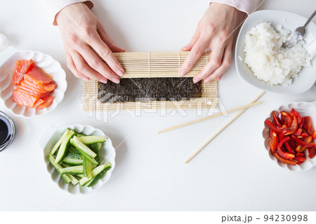 Sushi preparation process, the girl makes sushi with different flavors - fresh salmon, caviar, avocado, cucumber, ginger, rice. Sushi preparation process, the girl makes sushi with different flavors - fresh salmon, caviar, avocado, cucumber, ginger, rice. 94230998
