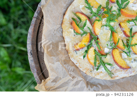 Very tasty and interesting pizza with peach and dor blue with arugula on parchment. Delicious, interesting taste of fruit pizza. Grilled pizza, outdoor recreation. Very tasty and interesting pizza with peach and dor blue with arugula on parchment. Delicious, interesting taste of fruit pizza. Grilled pizza, outdoor recreation. 94231126