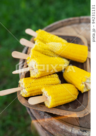 Boiled sweet corn with salt and butter on a stick on a wooden plate. Summer vegan dinner or snack, preparing for the grill. Vertical photo. Boiled sweet corn with salt and butter on a stick on a wooden plate. Summer vegan dinner or snack, preparing for the grill. Vertical photo. 94231131