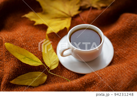 Still life with black coffee in a white cup that stands on a warm cozy sweater, top view, decorations with yellow leaves on the background. Still life with black coffee in a white cup that stands on a warm cozy sweater, top view, decorations with yellow leaves on the background. 94231248