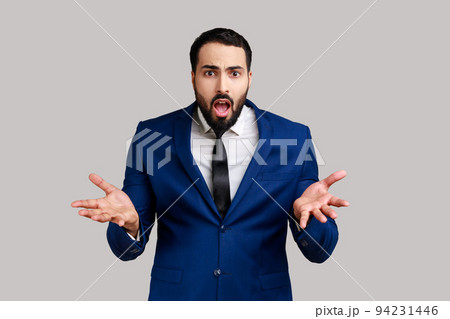 Portrait of bearded man standing with raised hands and indignant expression, asking reason of conflict, wearing official style suit. Indoor studio shot isolated on gray background. Portrait of bearded man standing with raised hands and indignant expression, asking reason of conflict, wearing official style suit. Indoor studio shot isolated on gray background. 94231446