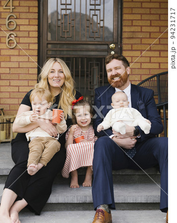 Portrait of parents with three children (2-5 months, 2-3) sitting on doorstep 94231717