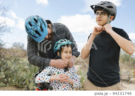 Father and children (8-9, 14-15) adjusting bike helmets Father and children (8-9, 14-15) adjusting bike helmets 94231746