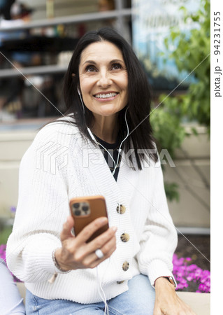 Smiling woman using phone and headphones 94231755