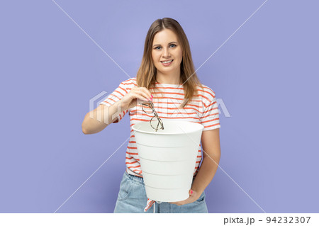 Portrait of blond woman wearing striped throwing out her optical glasses after laser vision treatment, being happy to have better eyesight. T-shirt Indoor studio shot isolated on purple background. Portrait of blond woman wearing striped throwing out her optical glasses after laser vision treatment, being happy to have better eyesight. T-shirt Indoor studio shot isolated on purple background. 94232307
