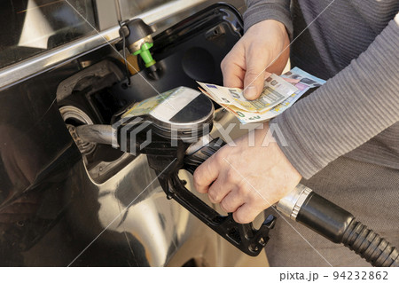 Car refuelling on petrol station. Man refilling car with fuel and holding money, euros. Close up. Gasoline, diesel is getting more expensive. Petrol industry and service. Petrol price and oil crisis. 94232862