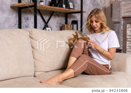 Thoughtful pensive woman sitting on sofa in modern white apartment, writing list to do in notepad using pen. 94233806