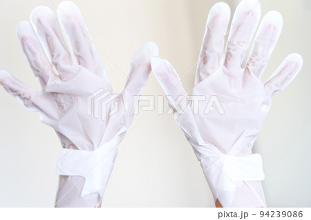 After a shower, a girl wrapped in a towel uses cosmetic gloves to moisturize the skin of her hands. Cosmetic trends for body care at home 94239086