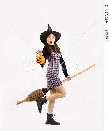 Halloween them, pretty asian girl in black dress holding broom and carrying pumpkin bucket posing on white background. 94239119
