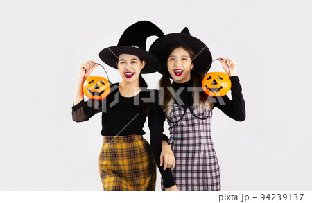Halloween theme, young asian woman in black costume witch hat holding and carrying orange pumpkin bucket and lantern posing happy smiling on white background. 94239137