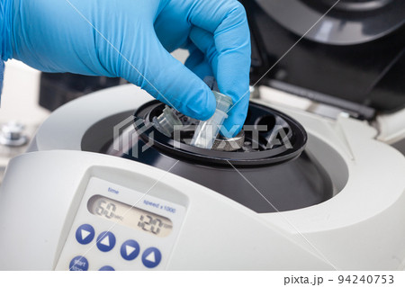 Closeup of a scientist hand placing a tube into an small table centrifuge. Spin column-based nucleic acid purification technique. Closeup of a scientist hand placing a tube into an small table centrifuge. Spin column-based nucleic acid purification technique. 94240753