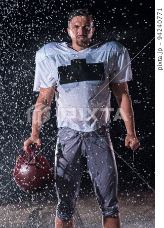 American Football Field: Lonely Athlete Warrior Standing on a Field Holds his Helmet and Ready to Play. Player Preparing to Run, Attack and Score Touchdown. Rainy Night with Dramatic Fog, Blue Light 94240771