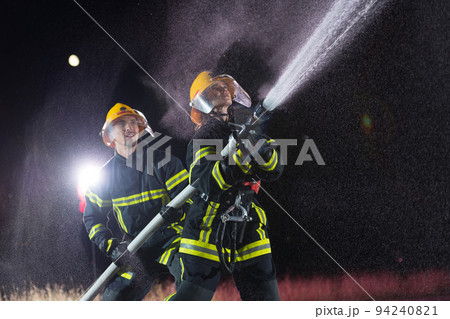 Firefighters using a water hose to eliminate a fire hazard. Team of female and male firemen in dangerous rescue mission. Firefighters using a water hose to eliminate a fire hazard. Team of female and male firemen in dangerous rescue mission. 94240821