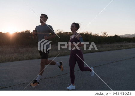 healthy young couple jogging in the city streets in the early morning with a beautiful sunrise in the background.  94241022