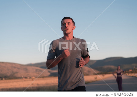 healthy young couple jogging in the city streets in the early morning with a beautiful sunrise in the background.  94241028