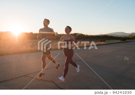 healthy young couple jogging in the city streets in the early morning with a beautiful sunrise in the background.  94241030