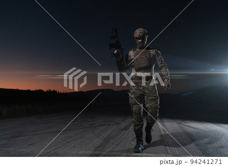 Army soldier in Combat Uniforms with an assault rifle, plate carrier and combat helmet going on a dangerous mission on a rainy night. Army soldier in Combat Uniforms with an assault rifle, plate carrier and combat helmet going on a dangerous mission on a rainy night. 94241271