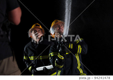 Firefighters use a water hose to eliminate a fire hazard. Team of firemen in the dangerous rescue mission. 94241478