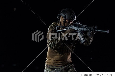 Army soldier in Combat Uniforms with an assault rifle, plate carrier and combat helmet going on a dangerous mission on a rainy night. Army soldier in Combat Uniforms with an assault rifle, plate carrier and combat helmet going on a dangerous mission on a rainy night. 94241714
