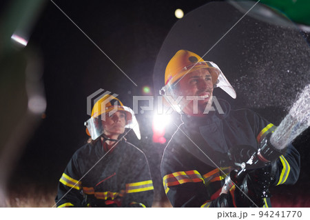 Firefighters using a water hose to eliminate a fire hazard. Team of female and male firemen in dangerous rescue mission. Firefighters using a water hose to eliminate a fire hazard. Team of female and male firemen in dangerous rescue mission. 94241770