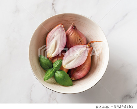 Whole and halved red eschalots in a bowl over white marble background. 94243265