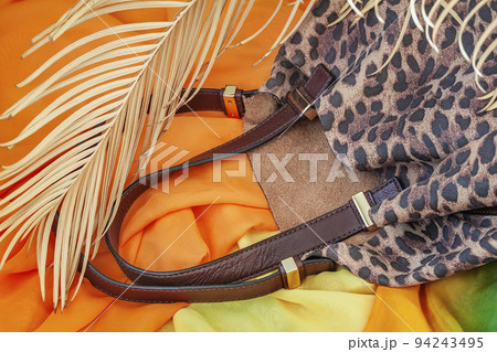 Handbag embossed under exotic skin of animal against background of bright stoles and tropical palm. Accessories concept Handbag embossed under exotic skin of animal against background of bright stoles and tropical palm. Accessories concept 94243495