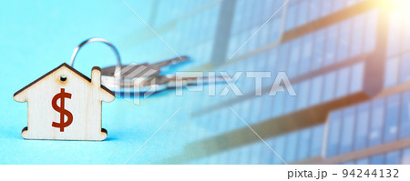Trinket in the form of a wooden house with the keys to the apartment against the backdrop of the facade of a modern building Trinket in the form of a wooden house with the keys to the apartment against the backdrop of the facade of a modern building 94244132