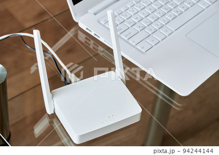 White wireless wi-fi router near a laptop on a glass table 94244144