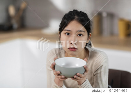 Starving asian woman holding empty plate next to mouth Starving asian woman holding empty plate next to mouth 94244465