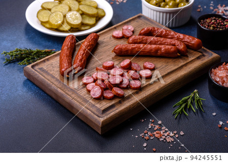 Delicious fresh smoked sausages cut with slices on a wooden cutting board 94245551