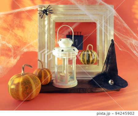 Halloween, a lantern with a burning candle, pumpkins, a witch's hat, against the background of a frame, cobwebs with spiders and magical shadows, the concept of interior decoration for the holiday Halloween, a lantern with a burning candle, pumpkins, a witch's hat, against the background of a frame, cobwebs with spiders and magical shadows, the concept of interior decoration for the holiday 94245902