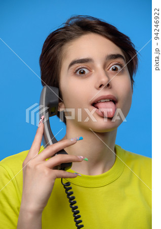 Beautiful young skinny brunette grimaces with tongue out while talkng on landline phone 94246922